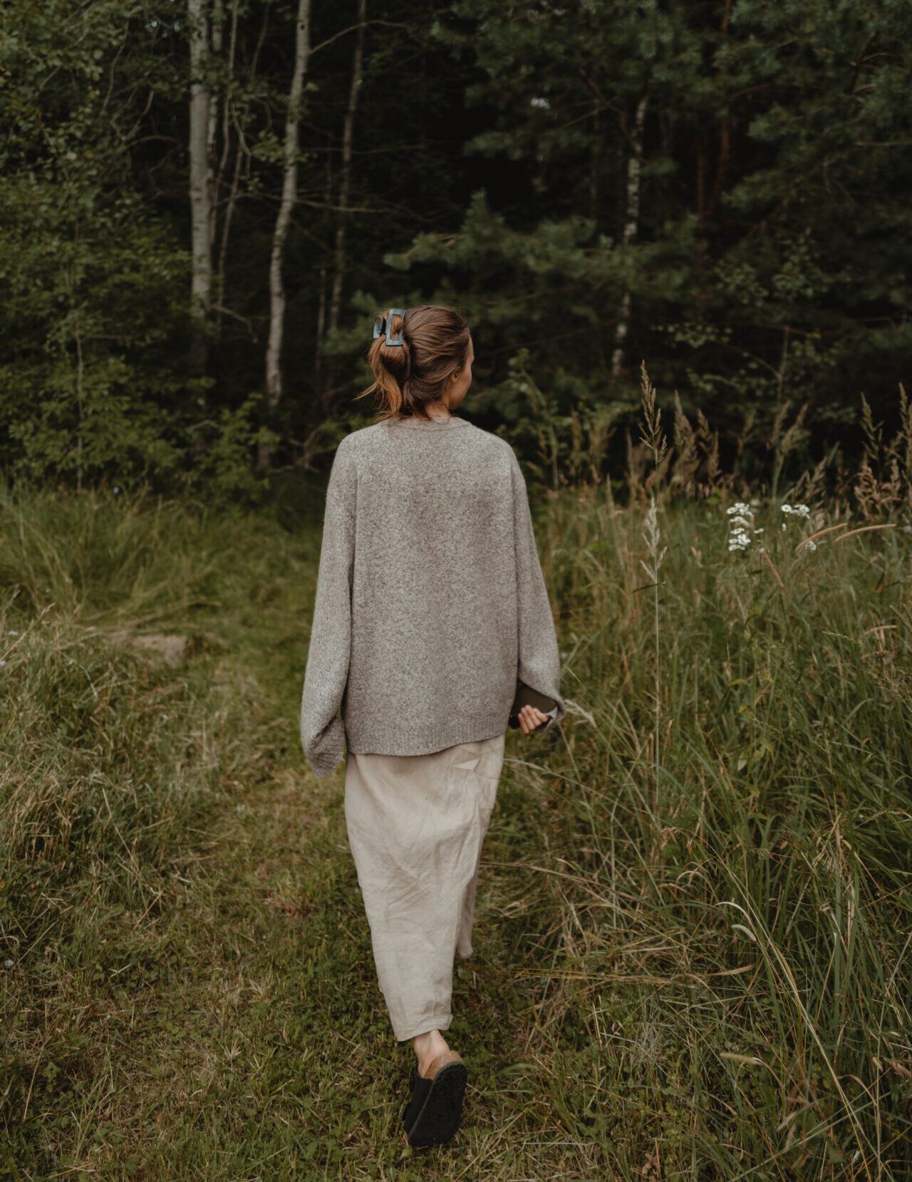 Eine Frau geht über eine Lichtung auf den Wald zu