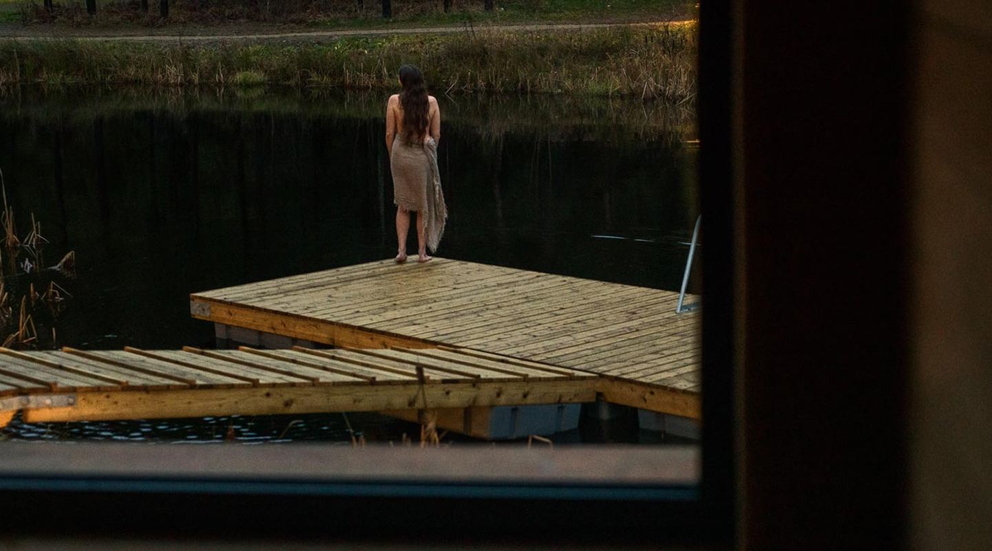 Eine Frau steht in der Dämmerung auf dem Holzsteg am Teich